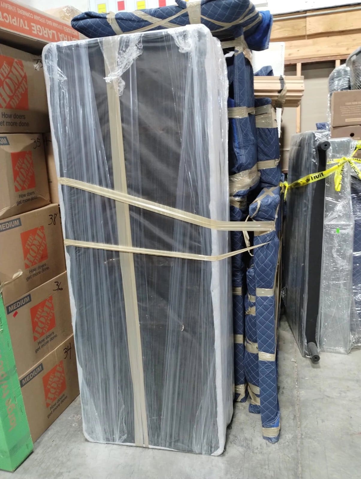 Wrapped mattress and blue quilted furniture in warehouse storage area next to Home Depot boxes
