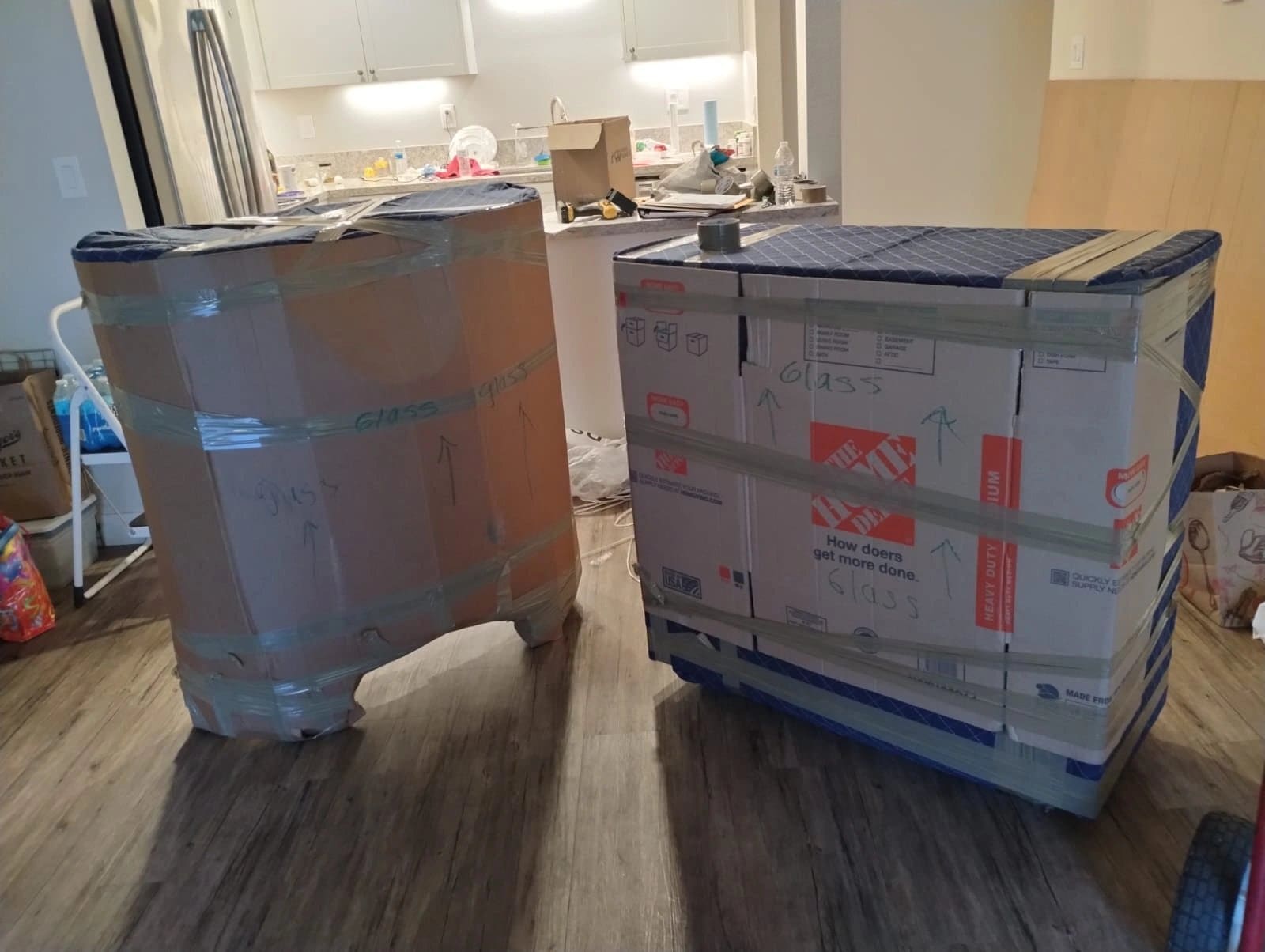 Large cardboard boxes and wrapped furniture in a kitchen during a move or renovation