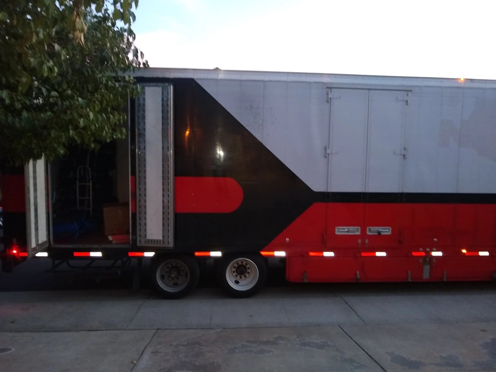 Red and black enclosed cargo trailer with dual rear axles parked on concrete