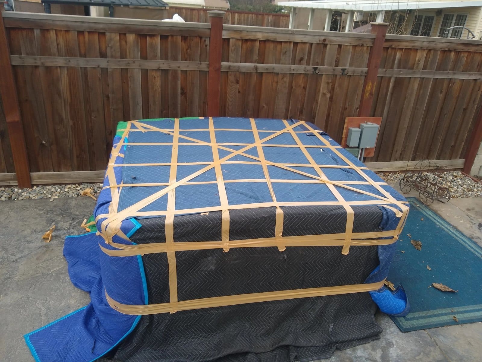 Cargo roof rack with tan straps securing rolled black mat on blue tarp in residential backyard
