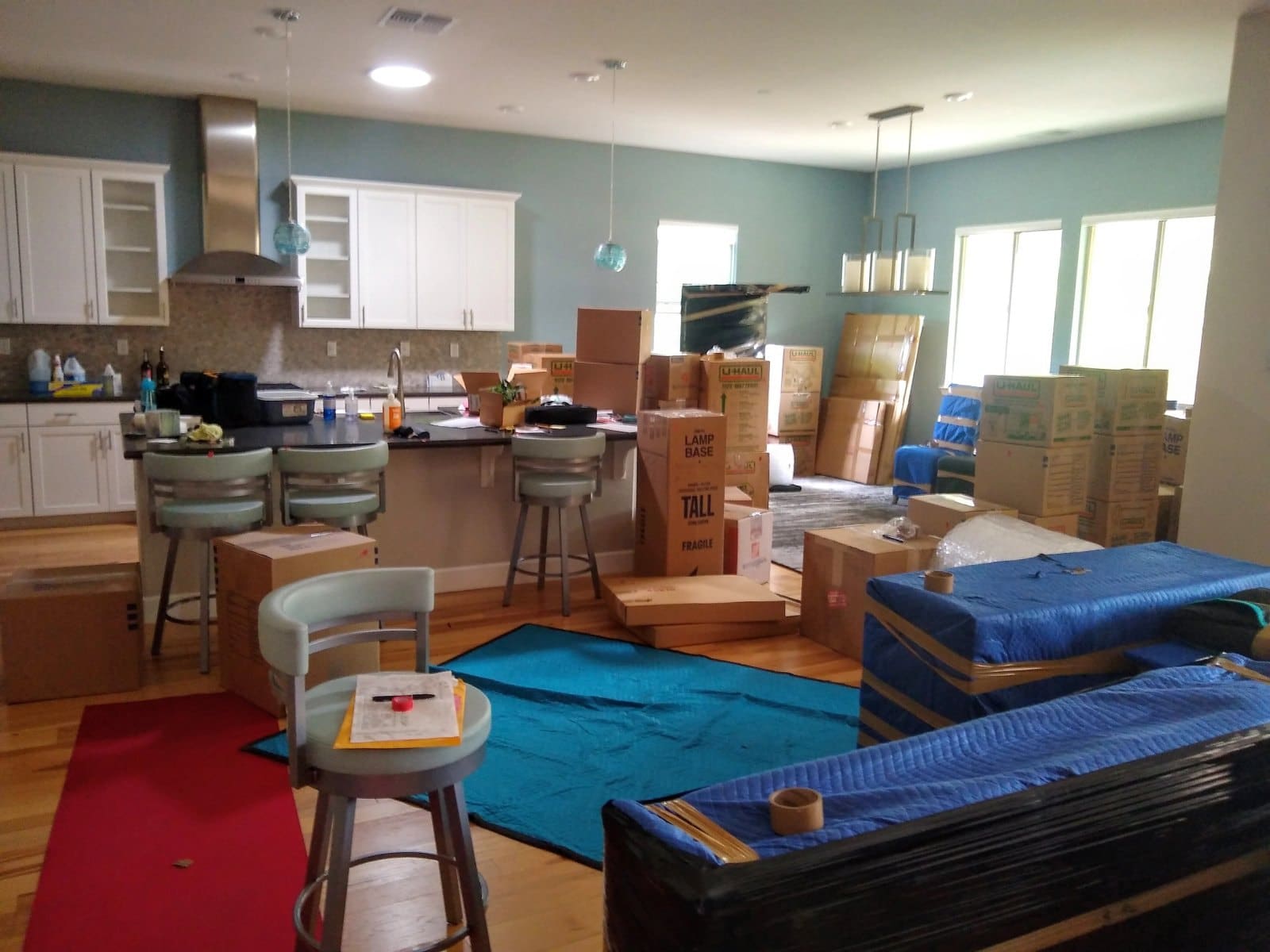 Moving day in modern home with kitchen, packed boxes, furniture in transit, and blue protective coverings
