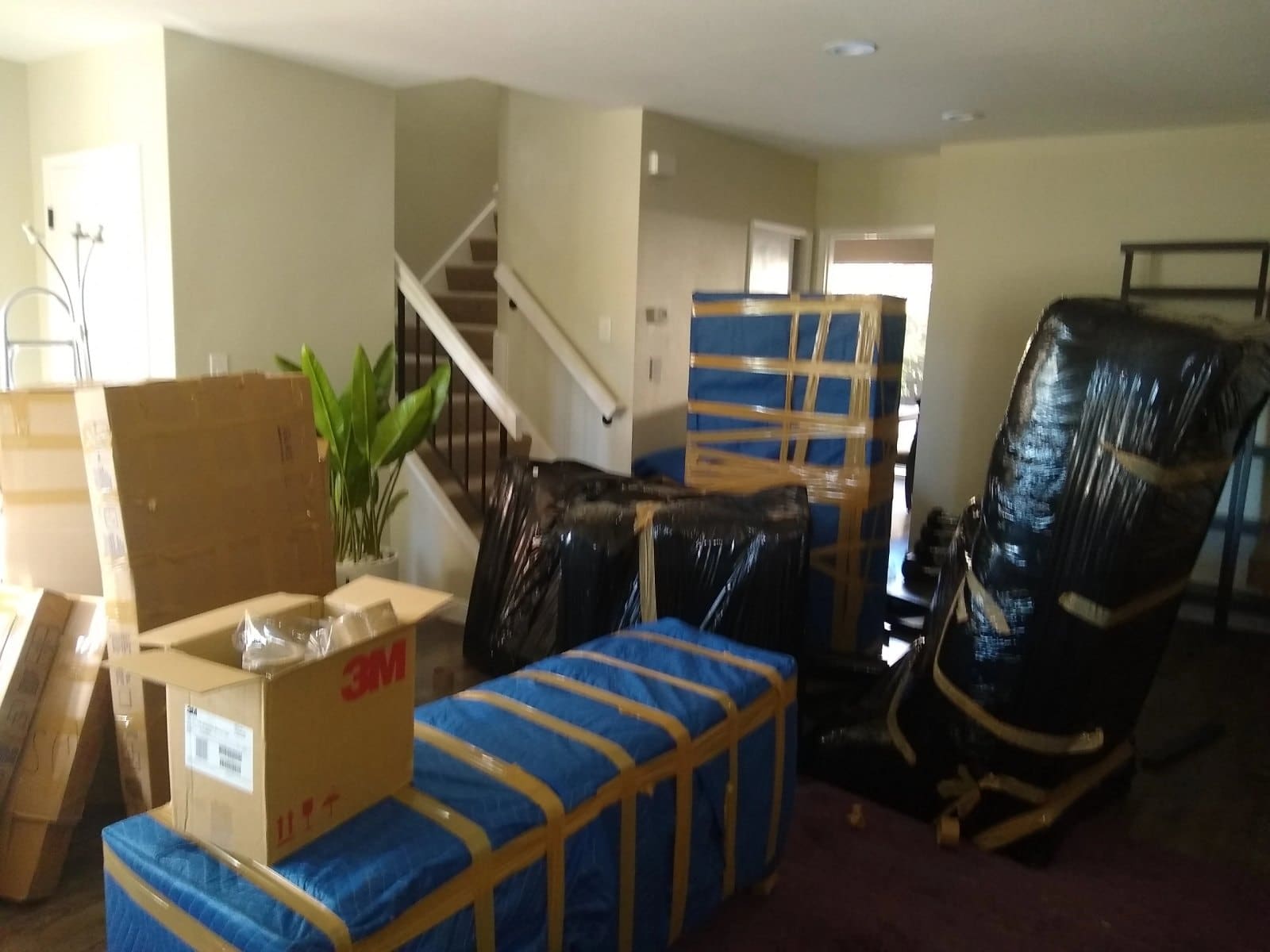 Moving boxes and wrapped furniture in residential entryway with stairs