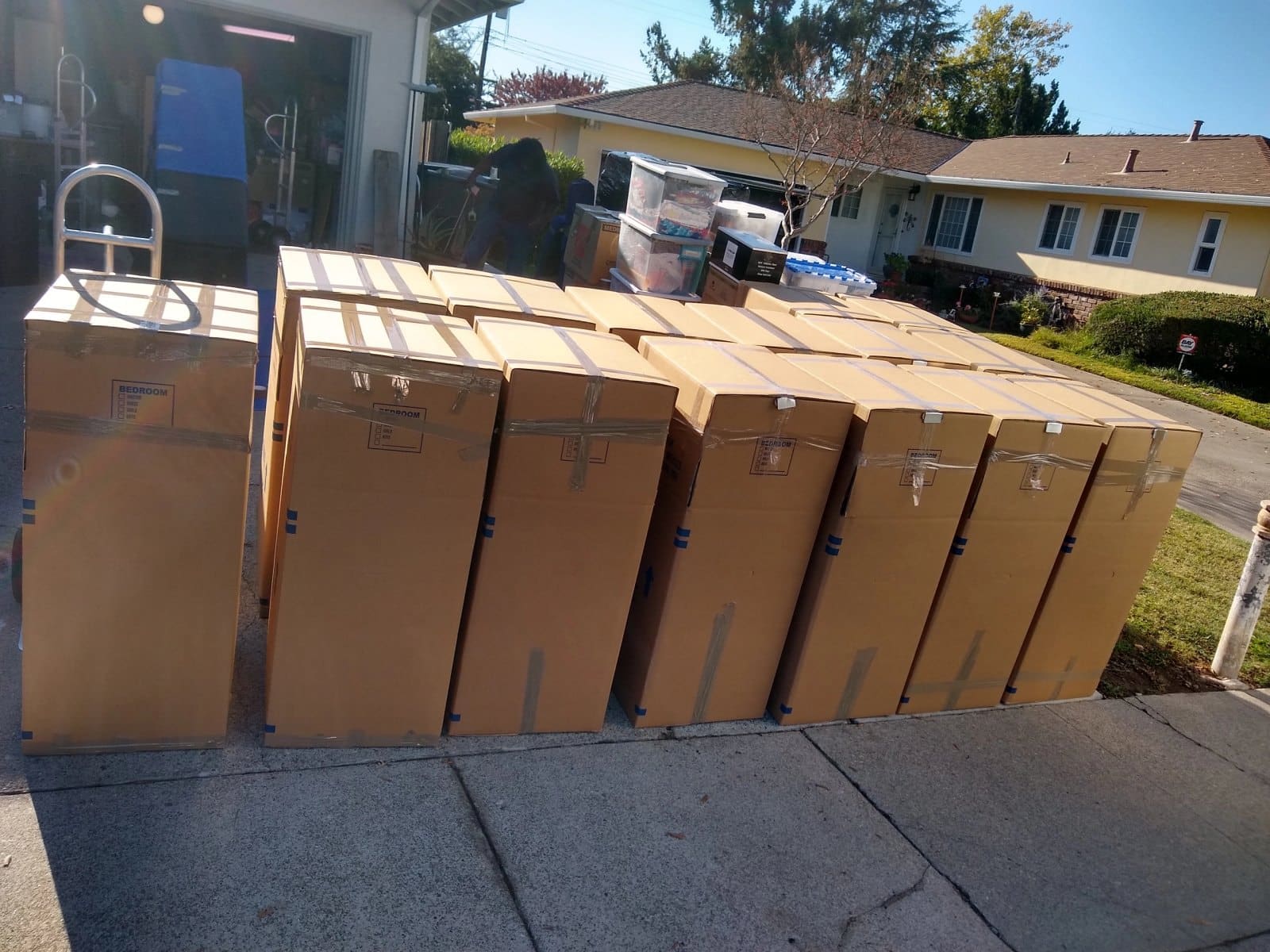 Row of seven large cardboard moving boxes lined up on a residential driveway