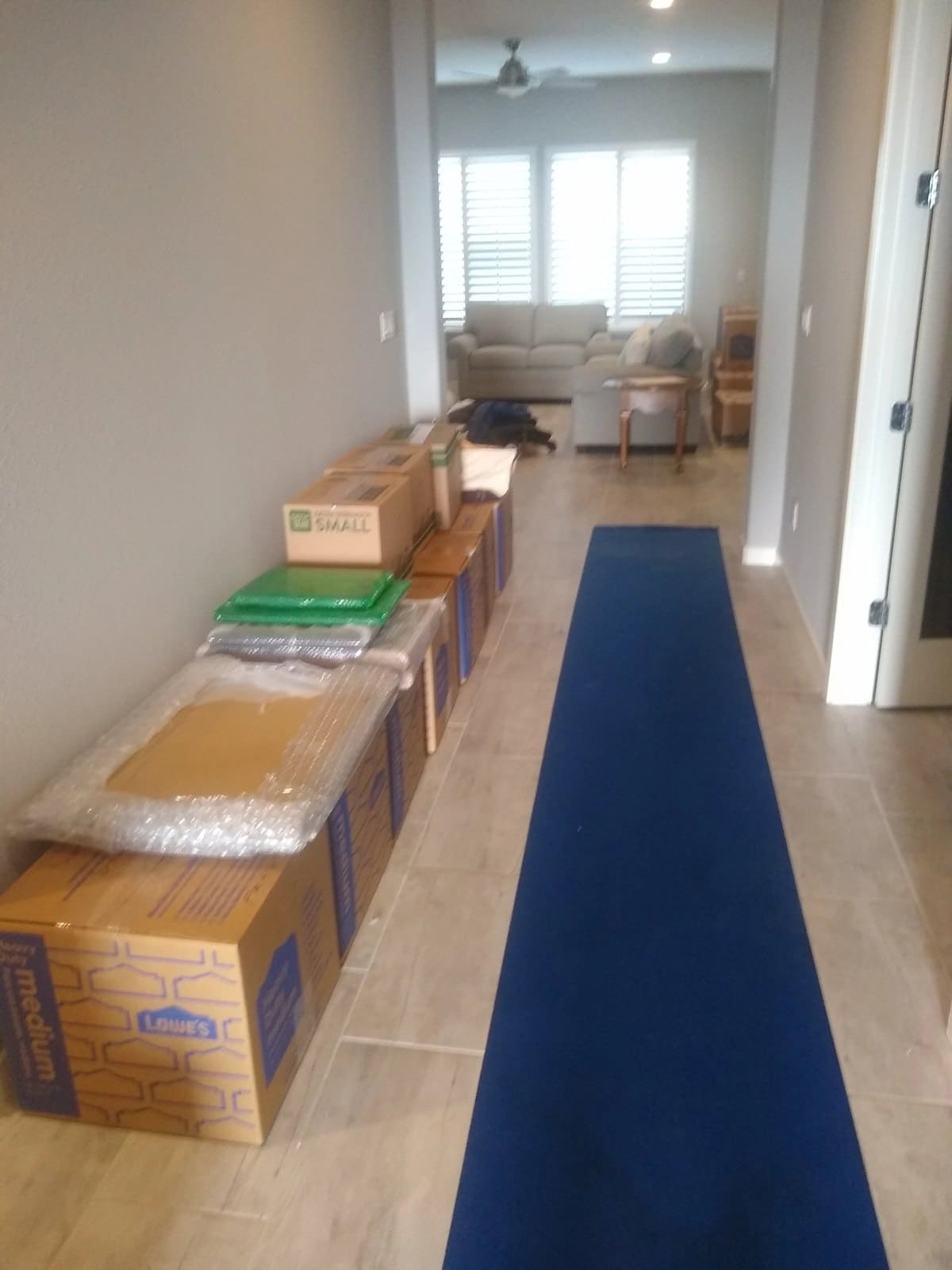 Hallway with stacked moving boxes and blue runner mat leading to living room