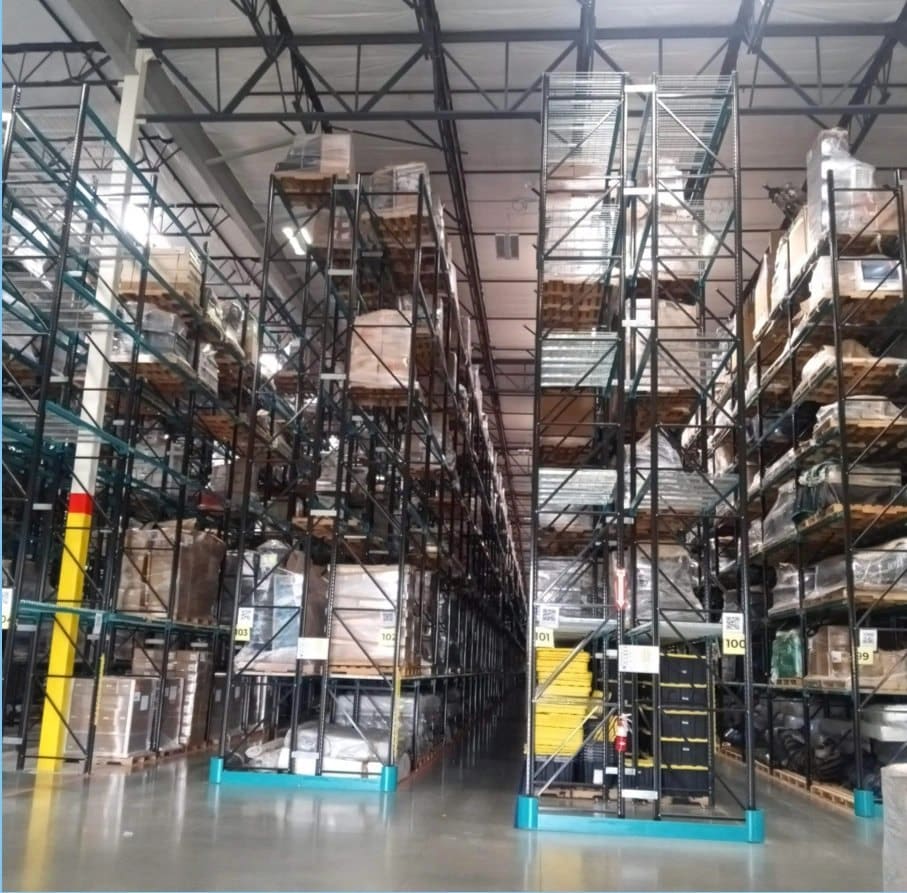 Industrial warehouse with tall metal shelving units stacked with brown boxes under bright overhead lighting
