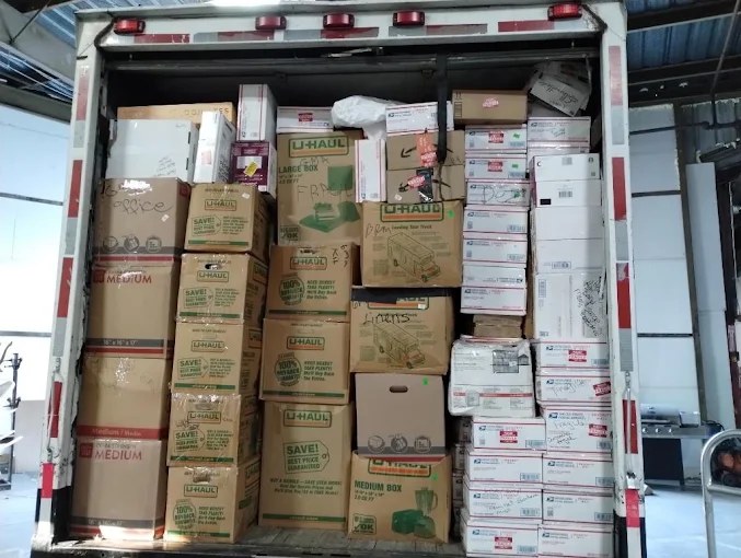 U-Haul moving truck cargo area packed with cardboard boxes and white shipping containers
