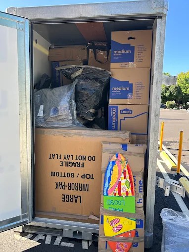 Packed moving truck with cardboard boxes, black bags, and safety equipment visible inside cargo area