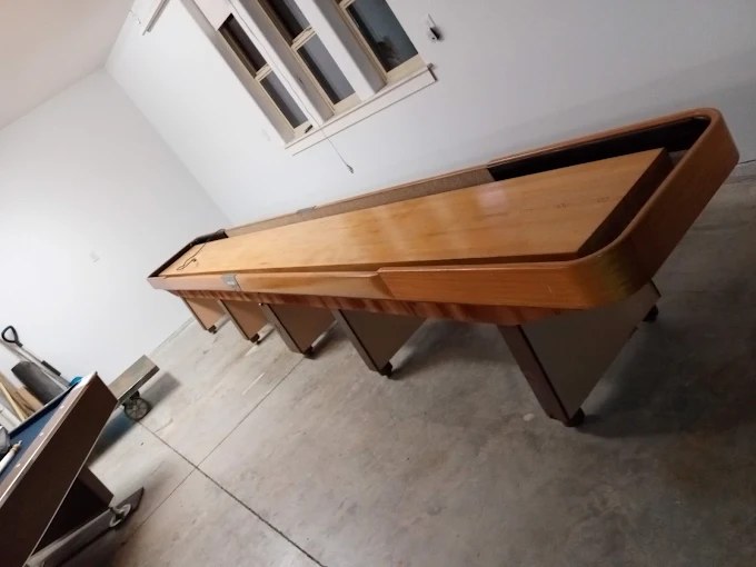 Wooden shuffleboard table with tan playing surface in warehouse setting