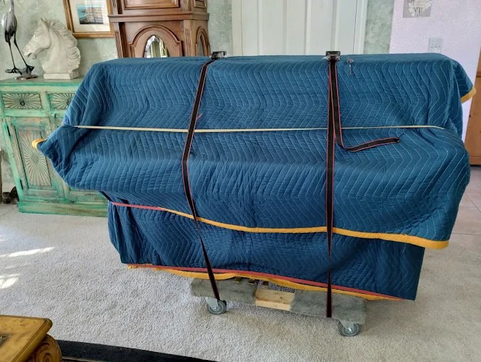 Blue upholstered couch wrapped with moving straps on wheeled dolly