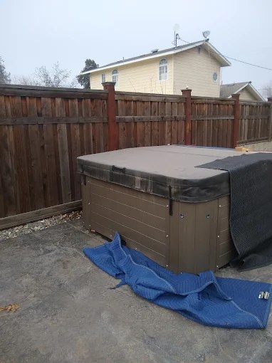 Hot tub with cover in backyard with wooden fence and house