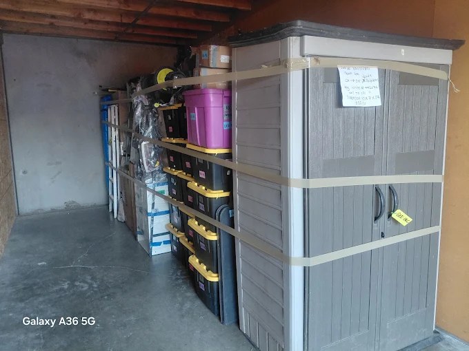 Garage storage area with black and yellow shelving units, gray plastic storage cabinet, and various tools and equipment
