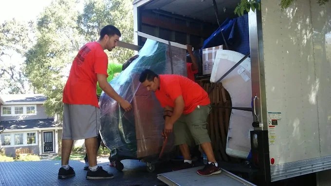 Two workers in red shirts loading furniture into a moving truck