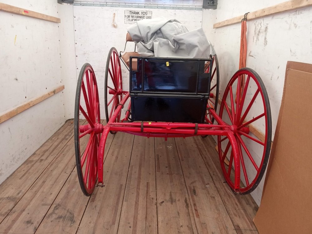 Red wagon with large spoked wheels and black cargo box stored indoors